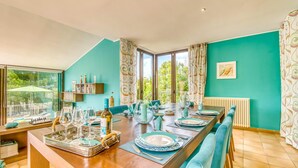 Un coin repas avec une longue table dressée pour six personnes, une bibliothèque et une vue sur la verdure à l’extérieur.