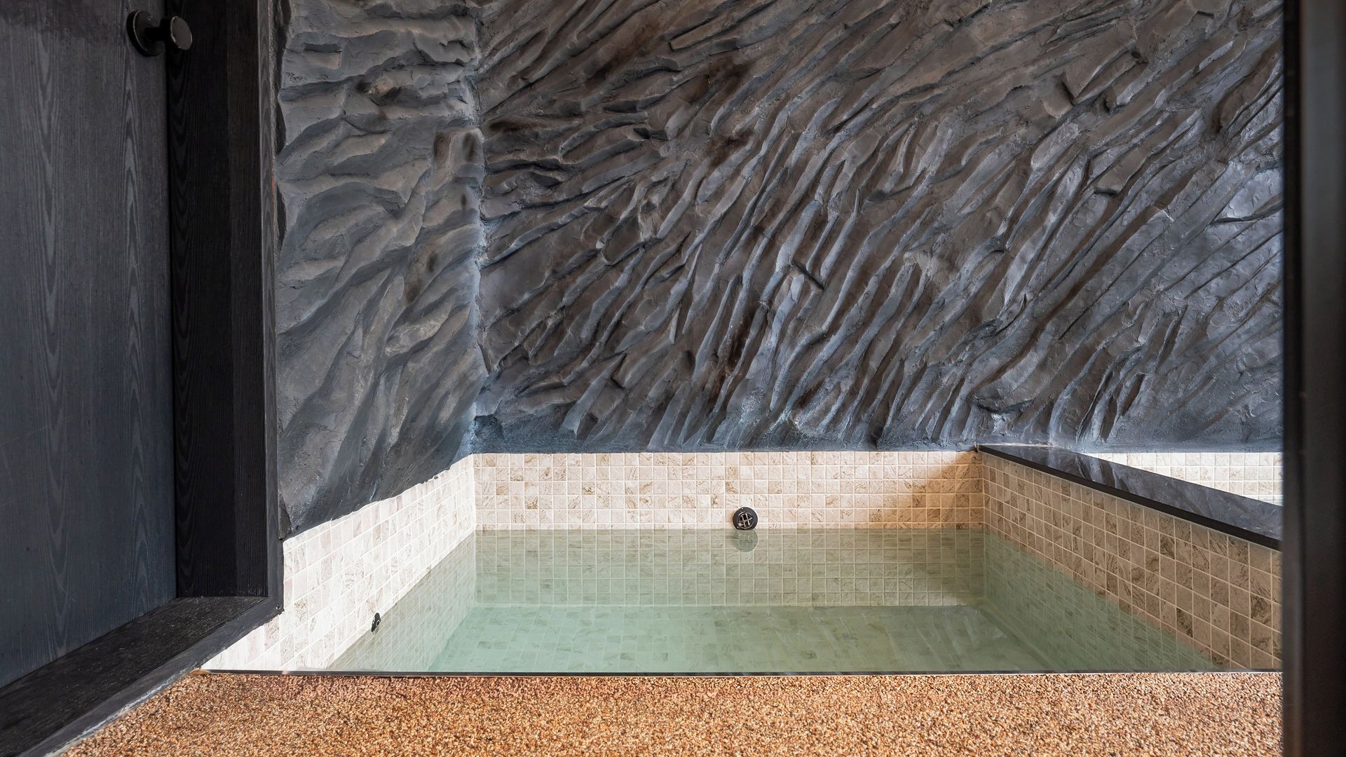 A spa room with a stone wall, a tiled floor, and a bathtub.