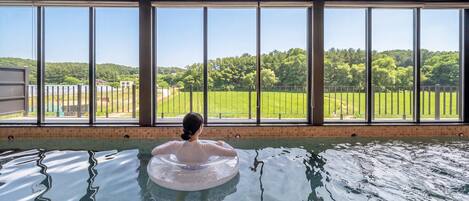 A person in a pool with a view of a green landscape through large windows.