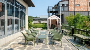 Een terras met buitenmeubilair, een overdekt gedeelte en een gebouw met grote ramen en een balkon.