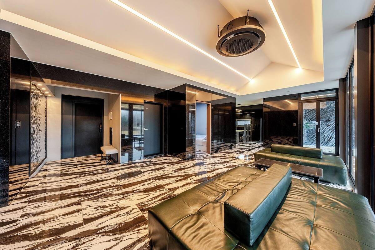 Een moderne hotelkamer met een marmeren vloer, een groene bank, een bed en een speaker in het plafond.