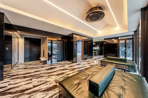 Een moderne hotelkamer met een marmeren vloer, een groene bank, een bed en een speaker in het plafond.