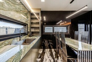A modern kitchen with a marble backsplash, built-in shelves, and a dining area with a unique chair design. - Gangneung Staymeet Private Pool Villa (Gangneung)