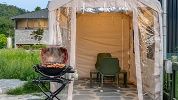 A tent with a grill, a chair, and a stone floor.