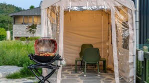 Une tente avec un barbecue, une chaise et un sol en pierre.