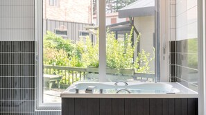Een moderne badkamer met een groot raam, een badkuip en uitzicht op een tuin.