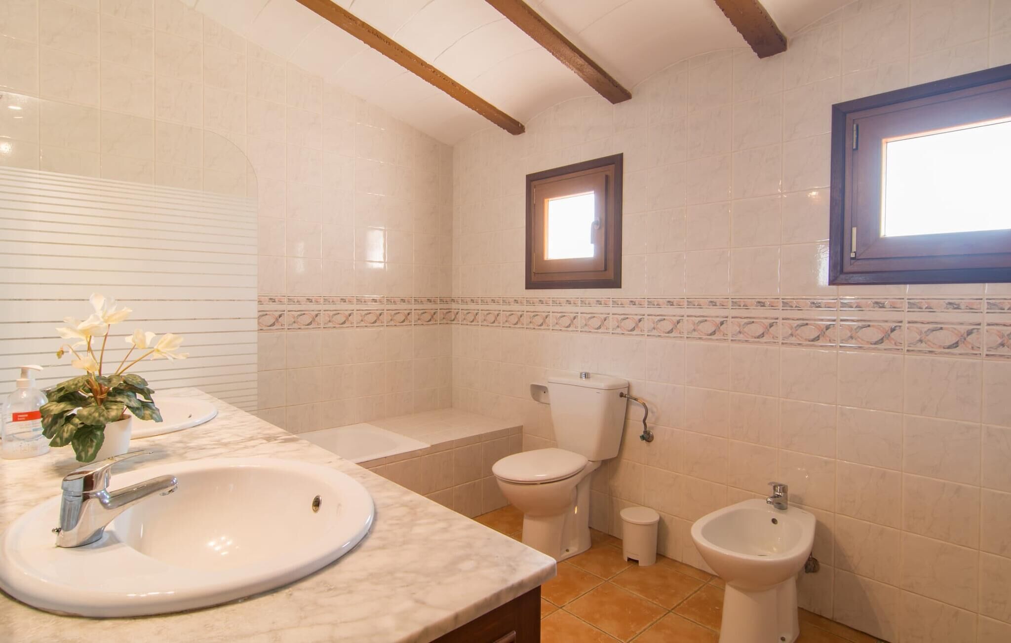 A bathroom with a sink, toilet, bidet, and a window.