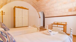 A bedroom with two beds, a wardrobe, a wooden dresser, and a window with a view.