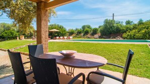 An outdoor patio with a table and chairs, a pool in the background, and a covered area with a pergola.