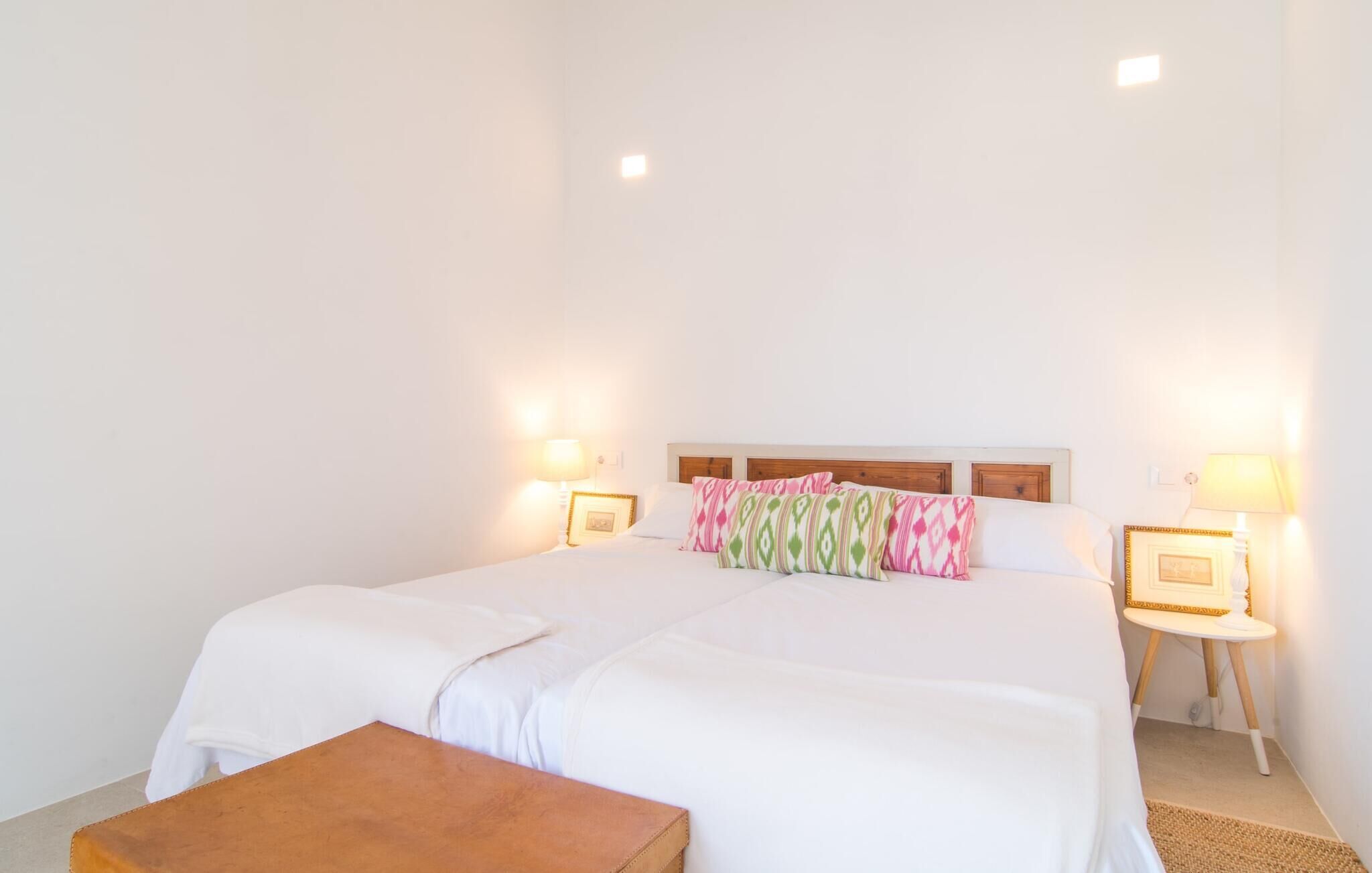Una habitación de hotel ordenada con una cama grande, dos mesitas de noche con lámparas y un pequeño banco de madera.