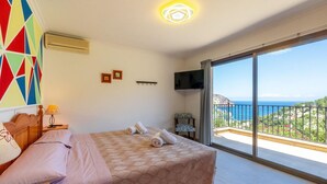Un dormitorio con cama, televisor, silla y balcón con vistas.