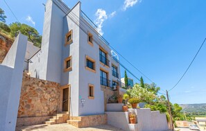 A multi-story building with a stone facade, a balcony, and a small garden area with potted plants. - Beach front home in Canyamel (Canyamel)