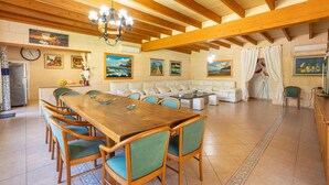 Amplia sala de estar con una mesa de comedor de madera, sillas tapizadas de verde, un sofá y una araña.