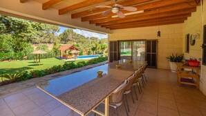 Un patio amplio con piscina, vigas de madera en el techo y vistas a un jardín exuberante y zona de piscina.
