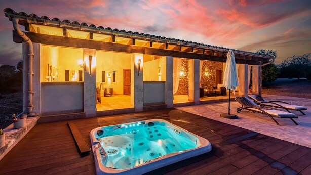 Un espace de détente extérieur moderne, doté d’un jacuzzi, d’une terrasse en bois et d’un coin salon abrité sous une pergola.