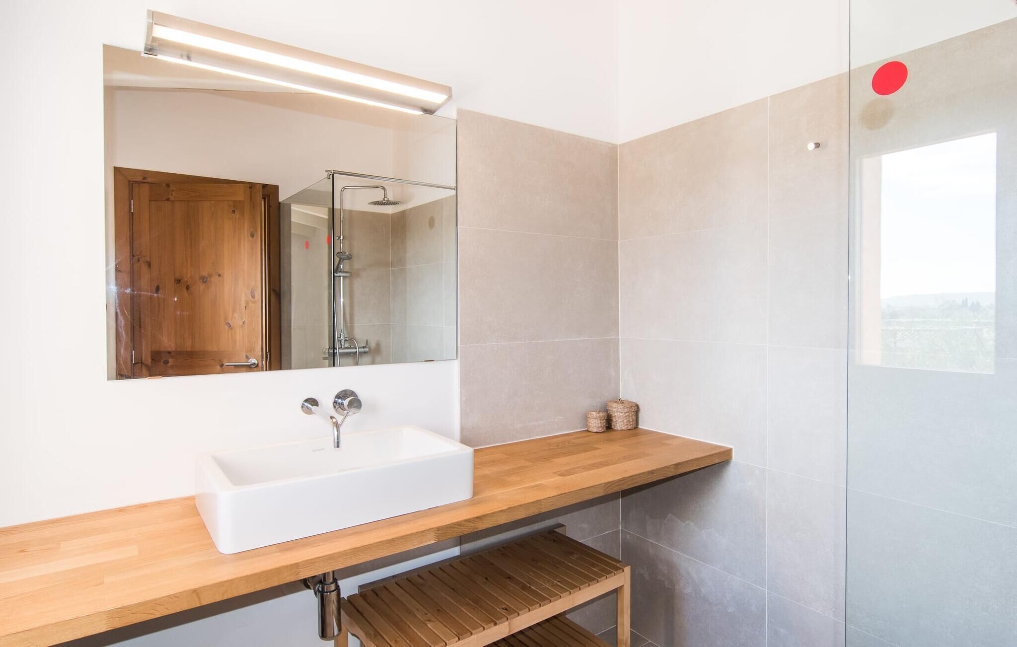 A modern bathroom with a wooden vanity, a white sink, a mirror, and a glass shower enclosure.