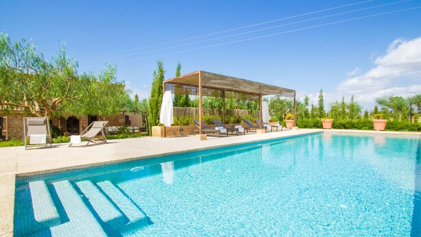 Ein Schwimmbad mit Liegestühlen und einer Pergola, umgeben von viel Grün.
