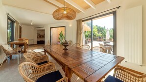 Un vaste espace dédié à la salle à manger, avec une table en bois et des chaises en osier, de grandes fenêtres ornées de rideaux et une vue sur la terrasse extérieure.