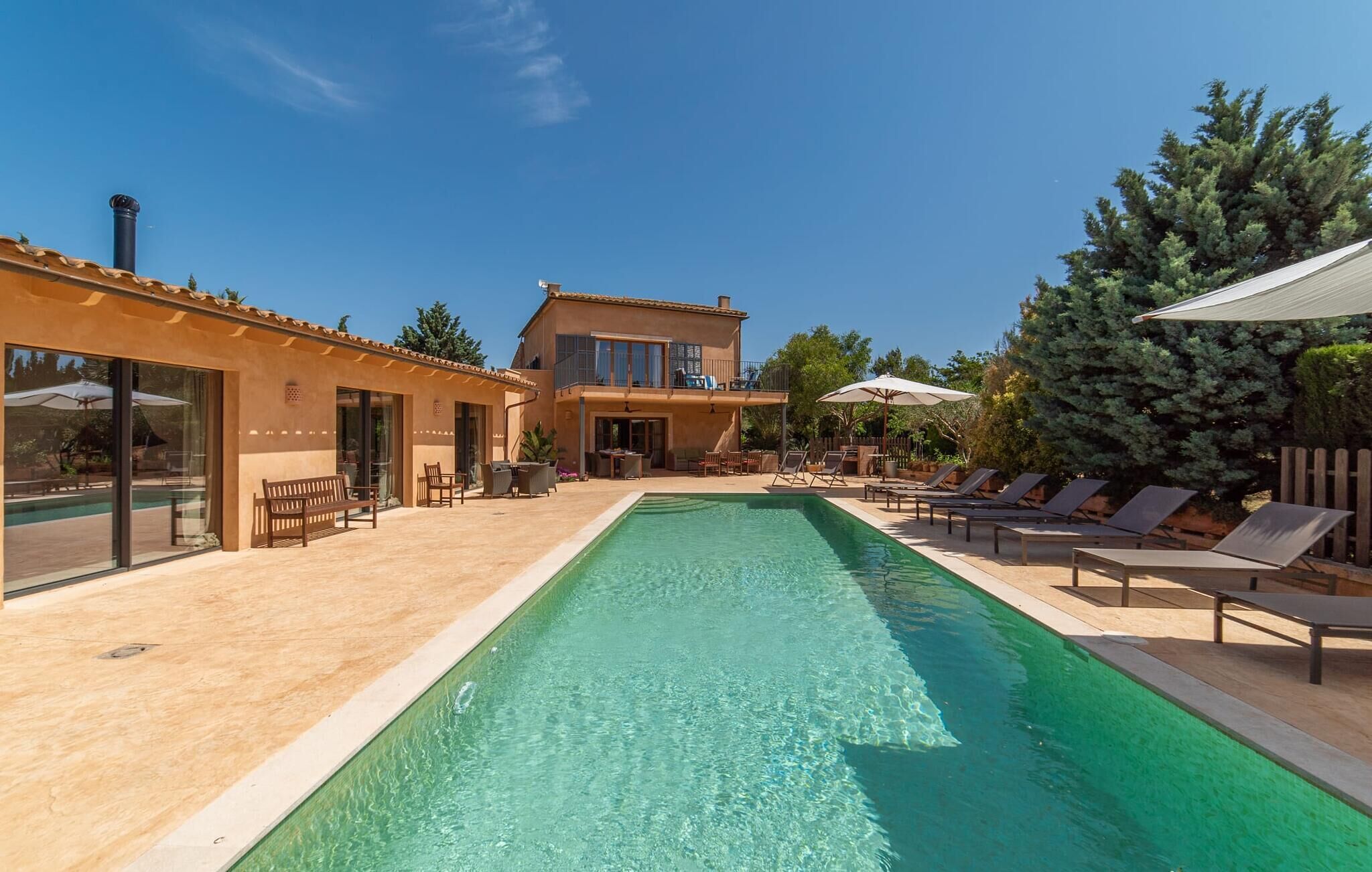 A poolside area with a clear pool, lounge chairs, and a building with large windows and a balcony.
