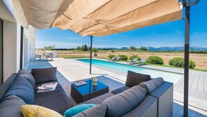 Un área junto a la piscina con un sofá, una mesa y una sombrilla grande.