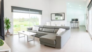 Una sala de estar moderna con un sofá seccional gris, una mesa de centro blanca y un ventanal con vistas a zonas verdes.