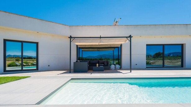 Un área de piscina moderna al aire libre con zona de estar cubierta, ventanas amplias y vistas al paisaje.