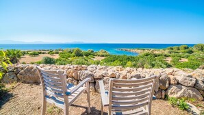 Two wooden chairs facing a stone wall overlooking a coastal landscape with a clear view of the sea and distant mountains. - Cozy home in Colonia de Sant Pere (Colonia de Sant Pere)