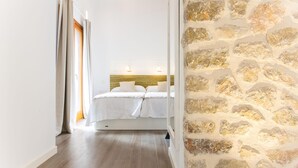 Ein Schlafzimmer mit Steinsandsteinwand, Holzboden und einem Bett mit weißen Leinen.
