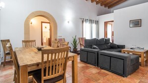 Ein gemütliches Wohnzimmer mit einem Holzesstisch, einer grauen Couch und einer Topfpflanze.