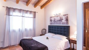 Ein Schlafzimmer mit Bett, Kopfstütze, Nachttisch, Stuhl, einem Gemälde und einer Tür.
