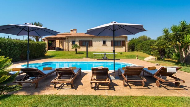 Ein Poolbereich mit Liegestühlen und Sonnenschirmen, ein Schwimmbecken und ein Haus im Hintergrund.