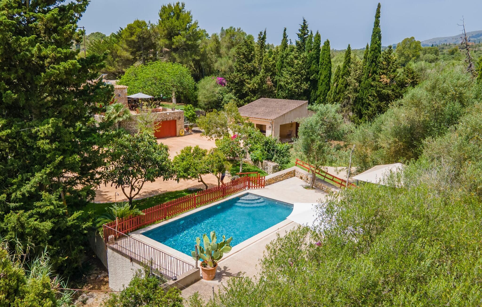 Ein Pool, umgeben von einem eingezäunten Garten mit Bäumen und einem kleinen Gebäude.