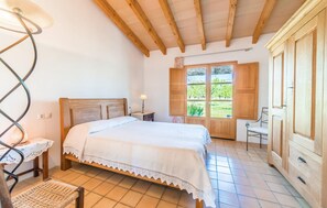 A bedroom with a wooden bed, a nightstand, a chair, and a window with a view of greenery. - Amazing home in Selva with private swimming pool, can be inside or outside (Selva)