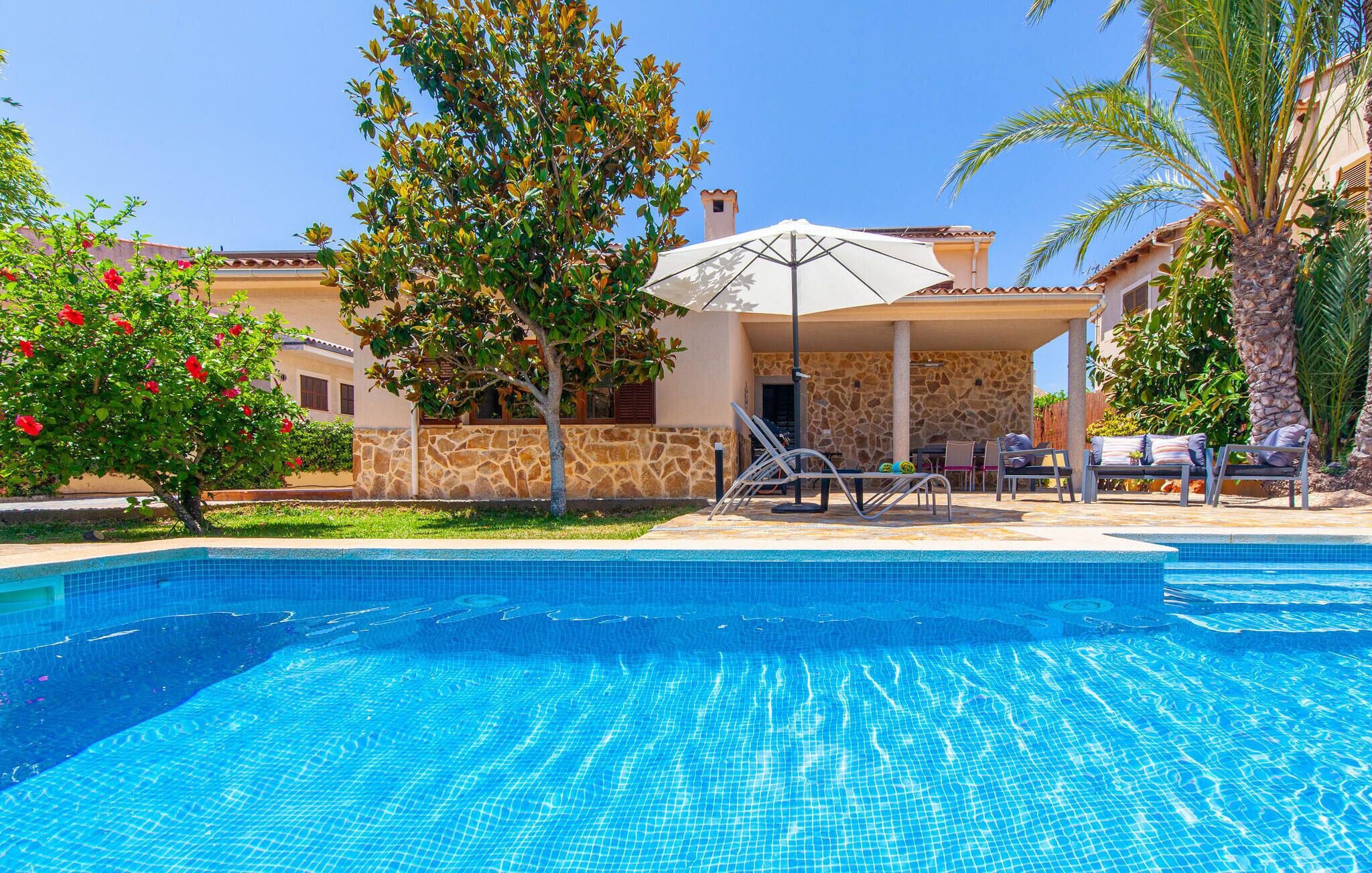 Una piscina con lettini e ombrelloni, circondata da muri in pietra e palme.