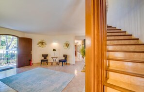 A spacious hallway with a wooden staircase, two chairs, a small table, and decorative wall art. - Amazing home in Sa Font de Sa Cala (Sa Font de Sa Cala)