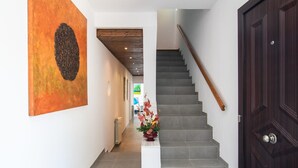 Un couloir avec un escalier, une porte en bois sombre et un grand tableau abstrait accroché au mur.