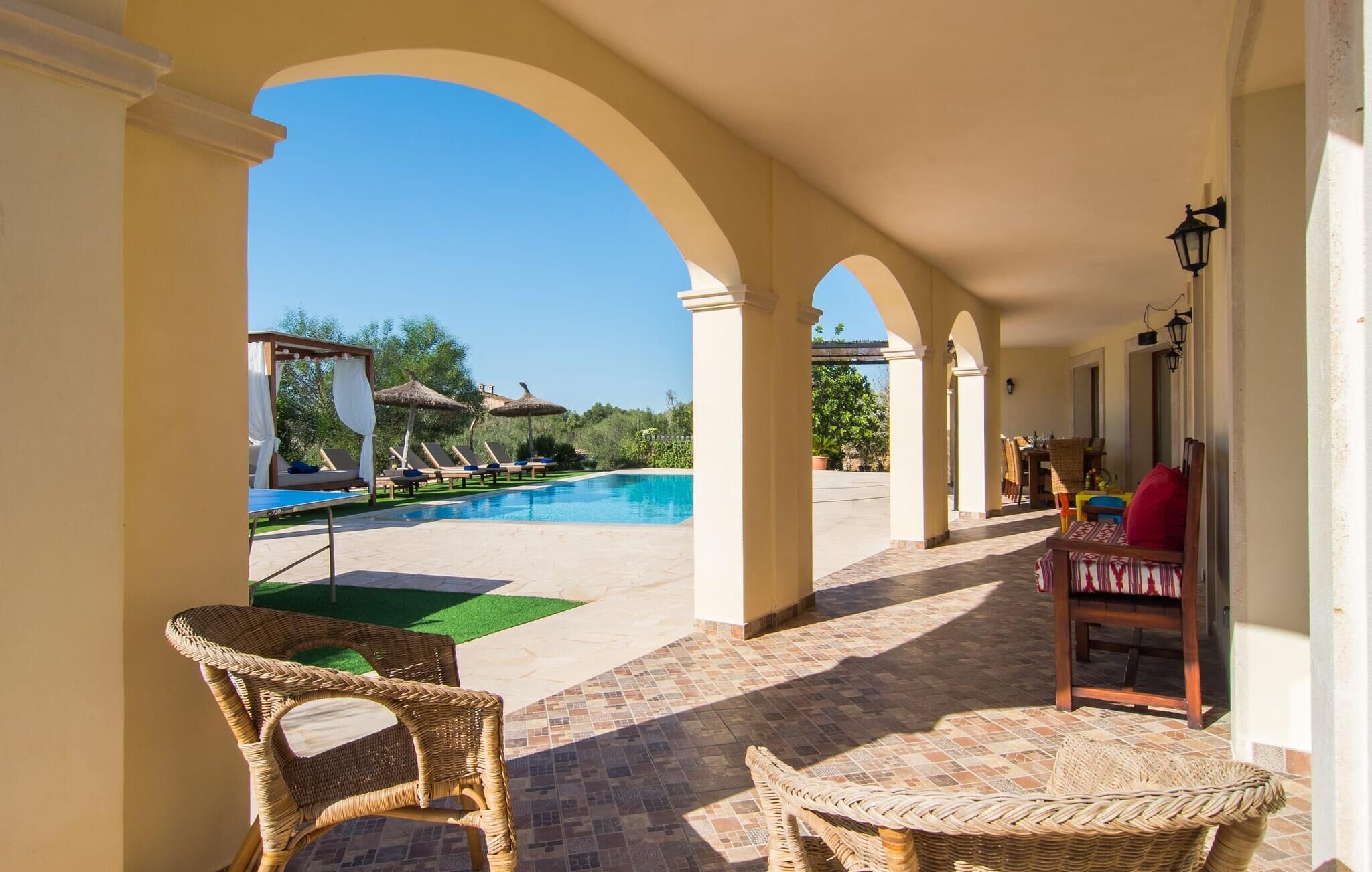 Un espacio al aire libre techado con piscina, sillones de descanso y mobiliario de mimbre.