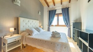 Ein Schlafzimmer mit Bett, Nachttisch, Lampe, Fernseher und einem Fenster mit Vorhängen.
