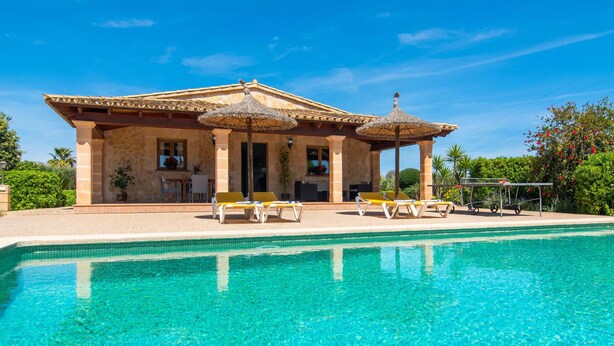 Un espace aménagé au bord de la piscine, avec une piscine à l’eau cristalline, des chaises longues et un patio couvert doté d’un toit en chaume.
