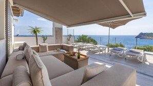 Un espace extérieur ensoleillé, aménagé avec des meubles de jardin, offrant une vue sur la mer et comprenant un canapé, des tables et des parasols.