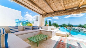 Ein sonniger Außenbereich mit Sitzgelegenheiten und Blick auf einen Pool, eine Holz-Pergola und eine Steinsitzbank.