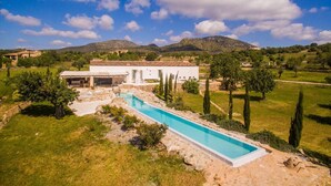 Eine moderne Villa mit Schwimmbad, umgeben von üppiger Vegetation und Bergen im Hintergrund.