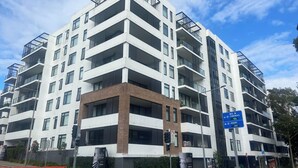 Een meerlaags woongebouw met balkons, een gevel van baksteen en een blauw bord met een richtingaanduiding.