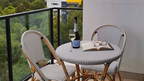 Een balkon met rieten stoelen, een tafel, een fles champagne en een glas.