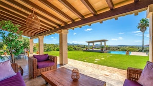 An outdoor patio with wicker furniture, a wooden table, and a view of a pool and landscape. - Awesome home in Son Macia with private swimming pool, can be inside or outside (Son Macia)