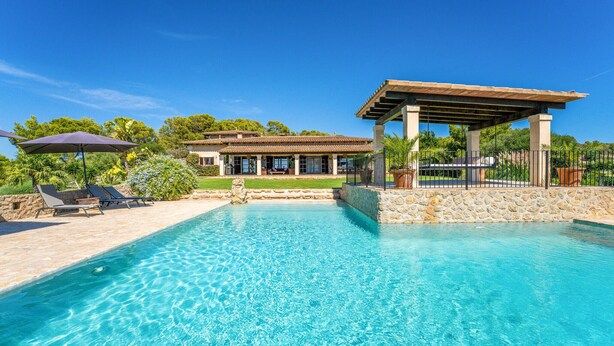 A clear swimming pool with lounge chairs and umbrellas, a covered patio, and a house with a tiled roof. - Awesome home in Son Macia with private swimming pool, can be inside or outside (Son Macia)