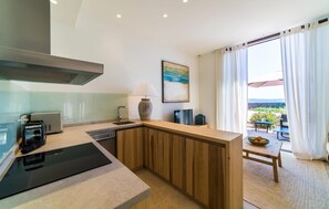 Eine moderne Küche mit Einbauherd, Spüle und einer Holztischinsel. Ein Gemälde ist an der Wand und durch große Fenster ist die Außenwelt sichtbar.