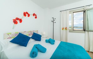 Habitación de hotel con cama, almohadas azules, manta azul y vista a la playa a través de la ventana.