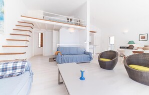A spacious living area with a high ceiling, a blue sofa, wicker chairs, and a white table. - 2 bedroom cozy home in Canyamel (Canyamel)