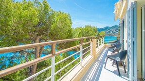 Un balcon doté d’une balustrade en bois, d’où l’on peut admirer une mer turquoise et des arbres verdoyants.
